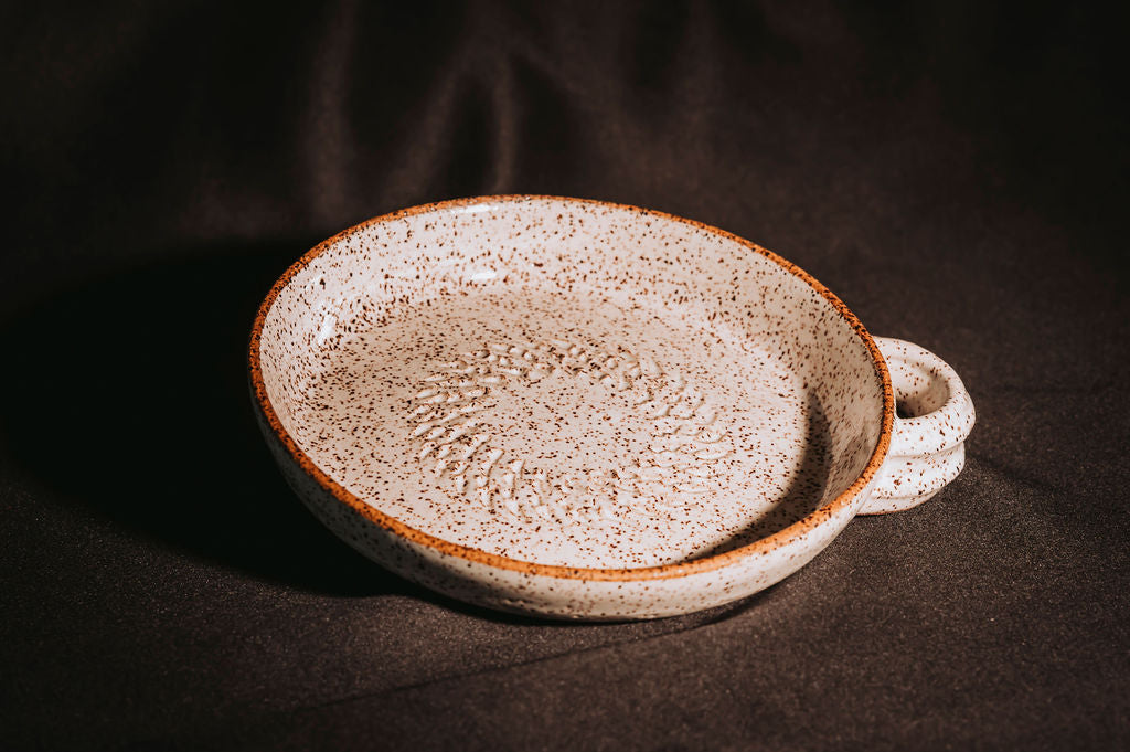 Ceramic garlic grater plate with textured surface on a dark background
