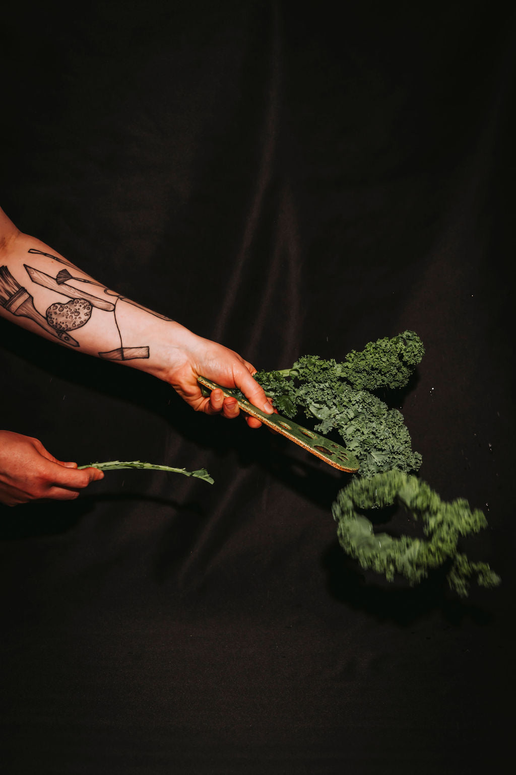 Person holding a bunch of green kale and using a ceramic herb stripper on a black background