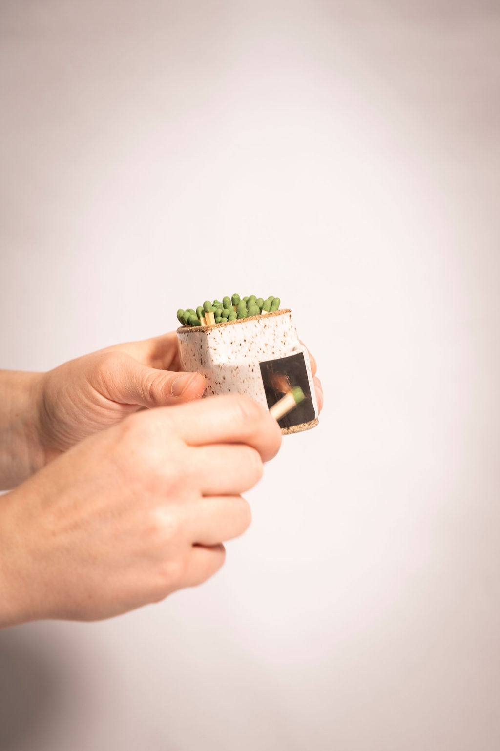 Person holding speckled white ceramic match holder and lighting a match on the side.