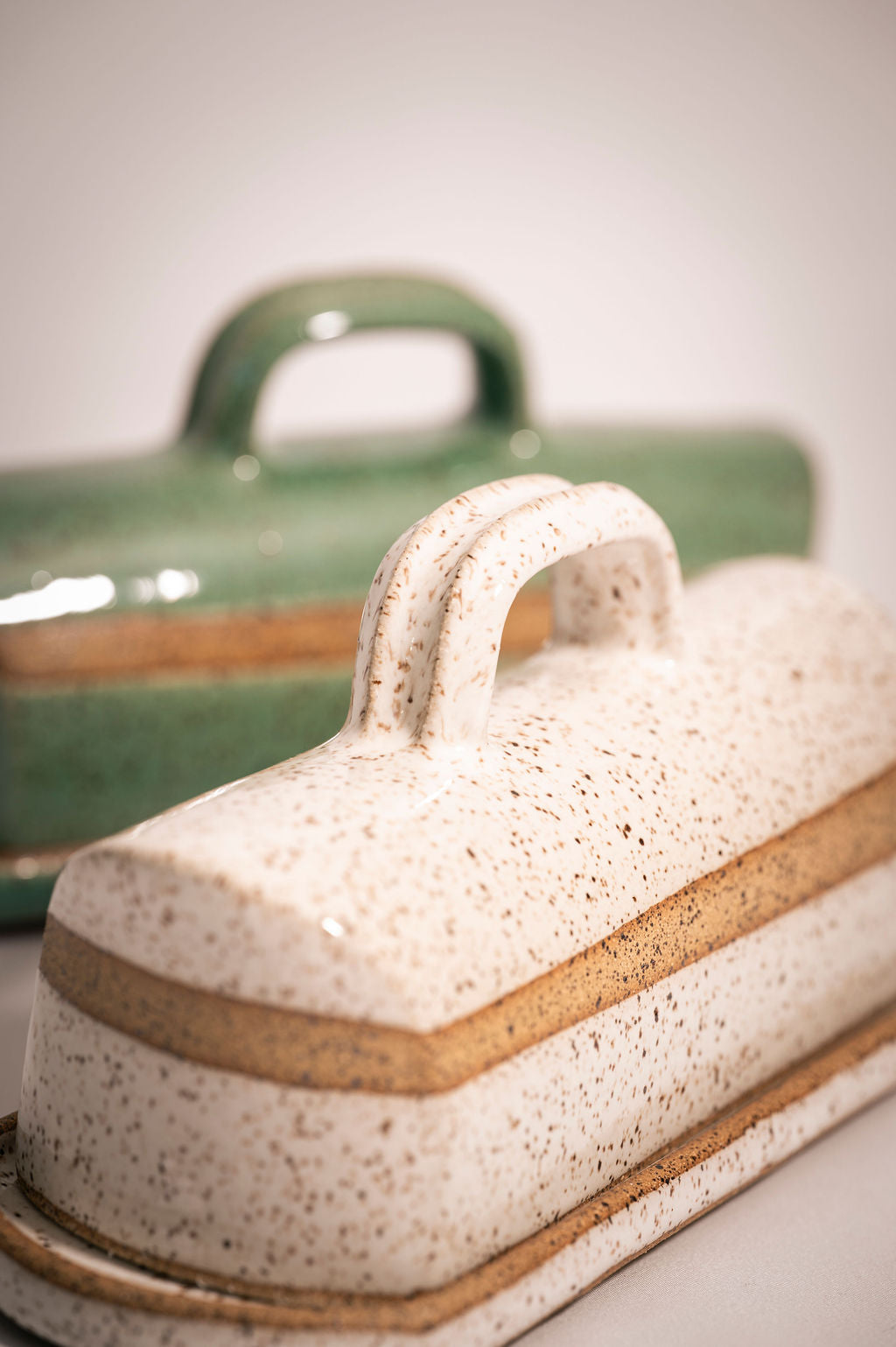 Close-up of a speckled white ceramic butter dish with a turquoise ceramic container in the background.