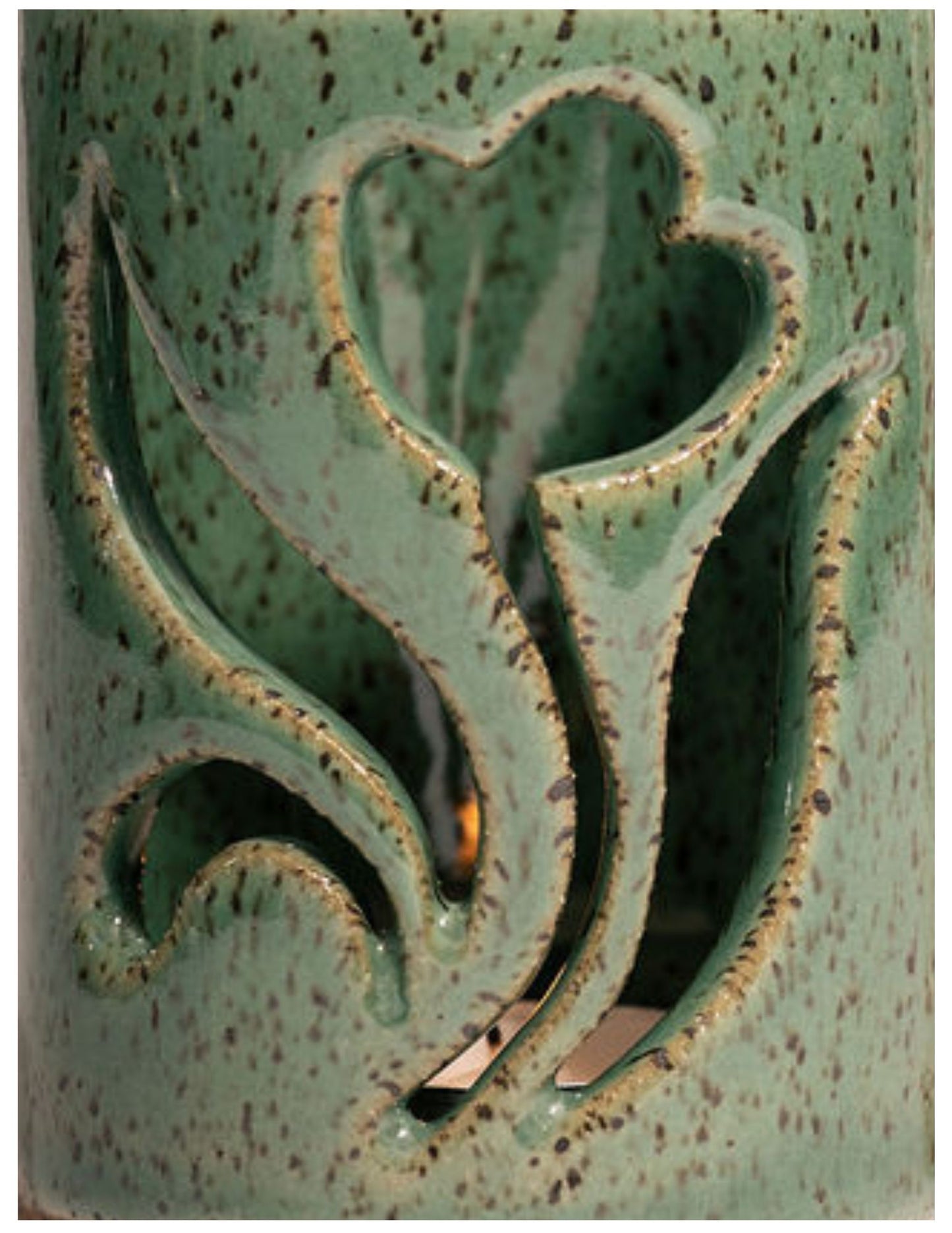 Decorative ceramic vase with floral cutout design on a speckled green surface