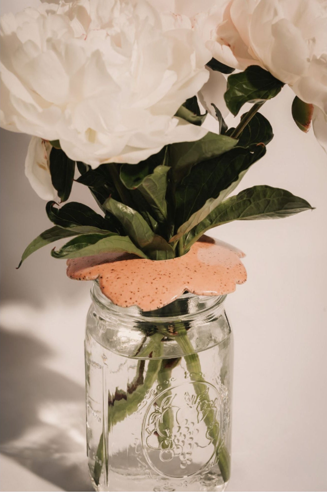 Bouquet of flowers in a glass mason jar with a decorative ceramic flwoer frog helping to arrange the flowers.