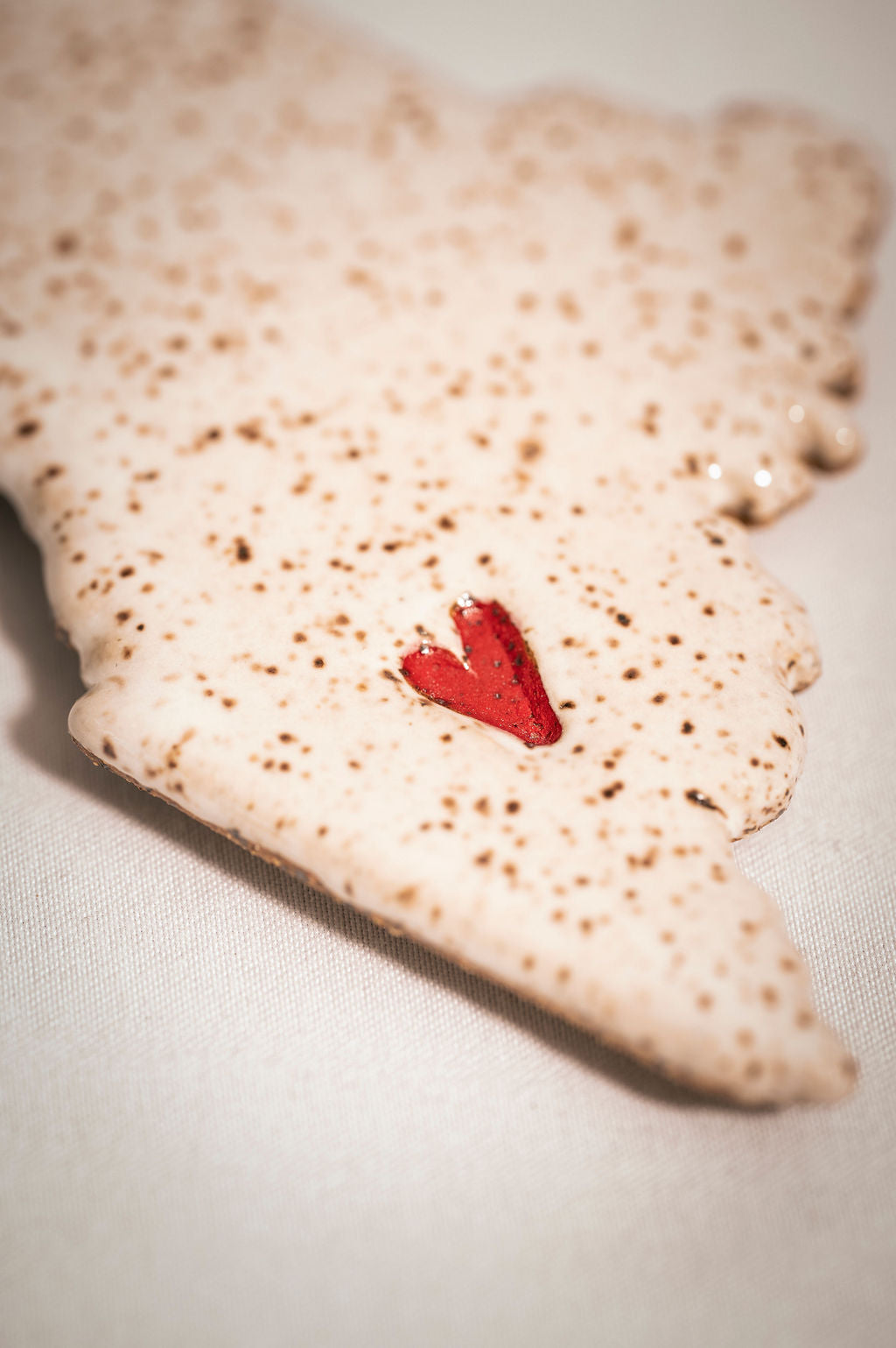Close up of a red heart shape on a speckled white ceramic magnet.