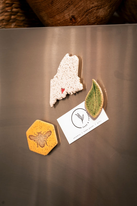 Three decorative magnets on a metallic fridge surface with a Sage & Sonder business card.