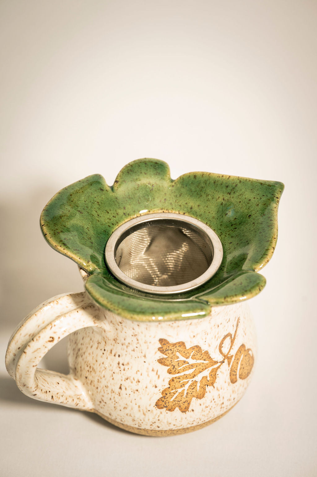 Ceramic mug with green leaf-shaped tea strainer resting on top.