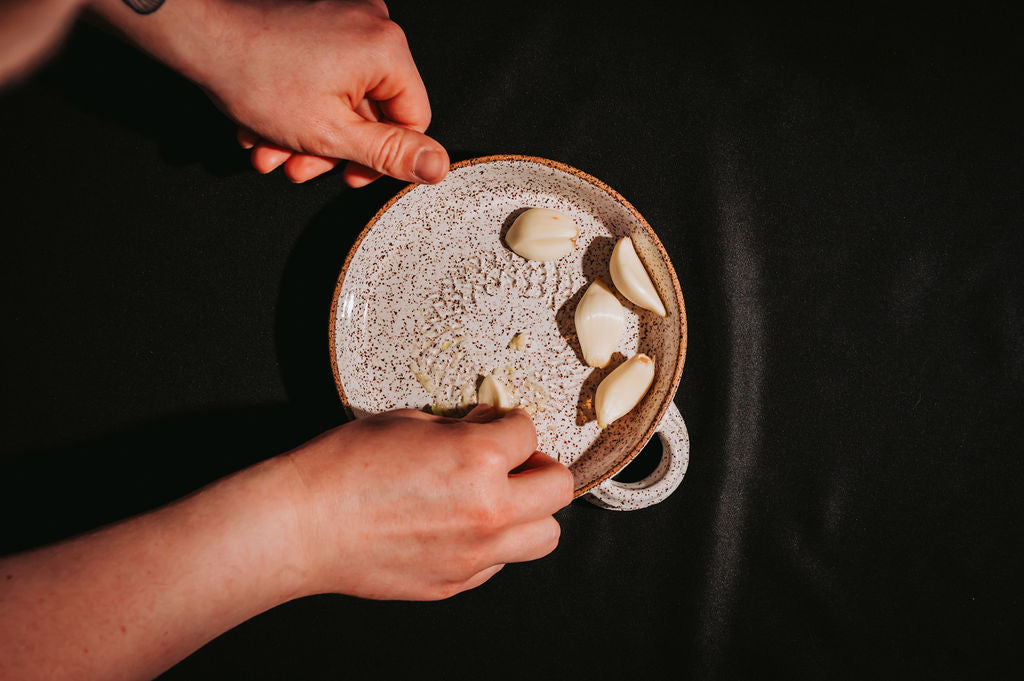 Person holding a ceramic plate with garlic cloves against a dark background