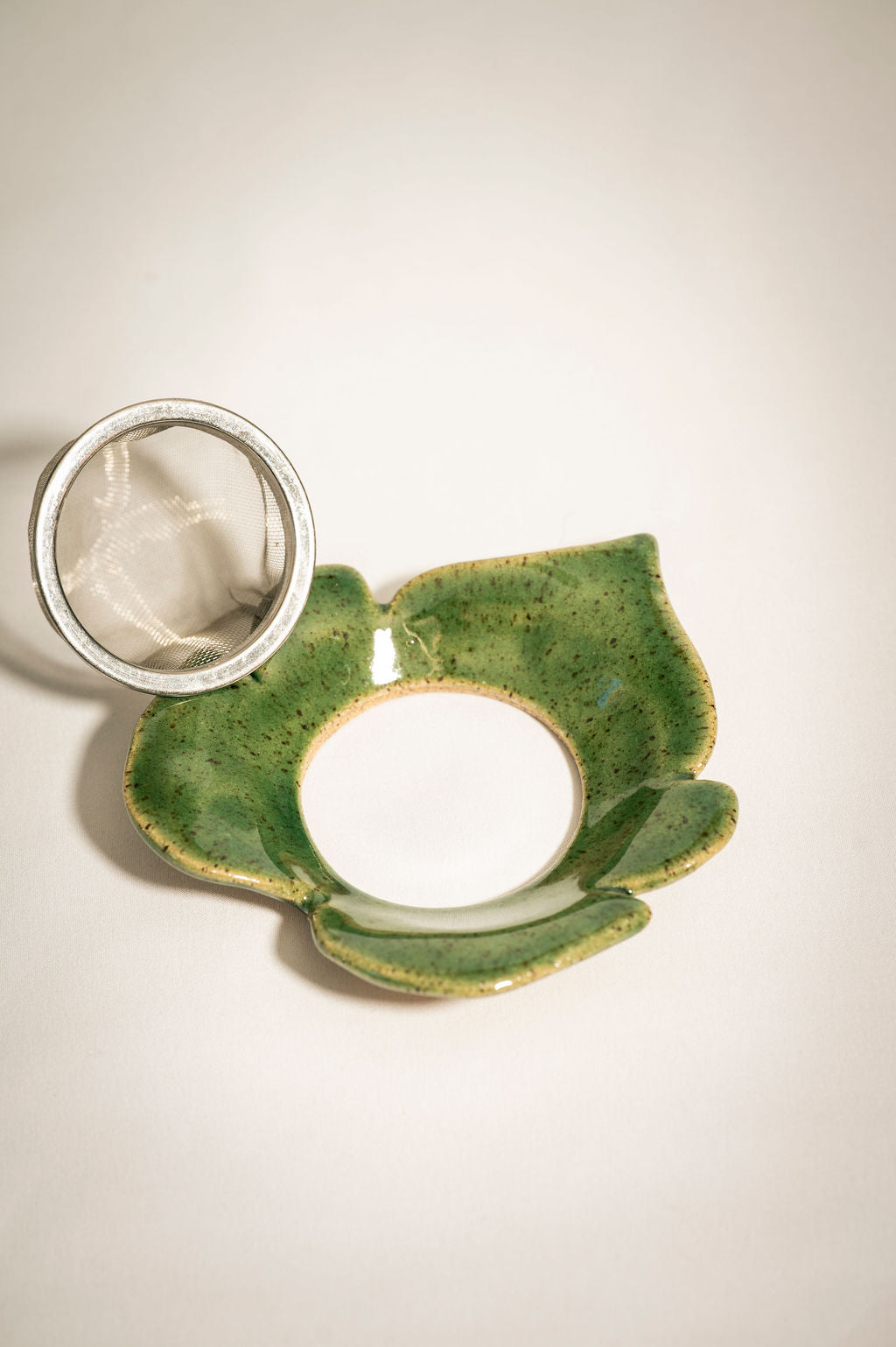 Green ceramic tea infuser in the shape of a leaf with a silver mesh tea strainer basket sitting next to it.