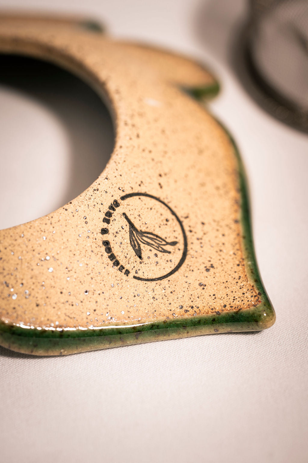 Back detail shot of a ceramic tea infuser in the shape of a leaf showing logo.