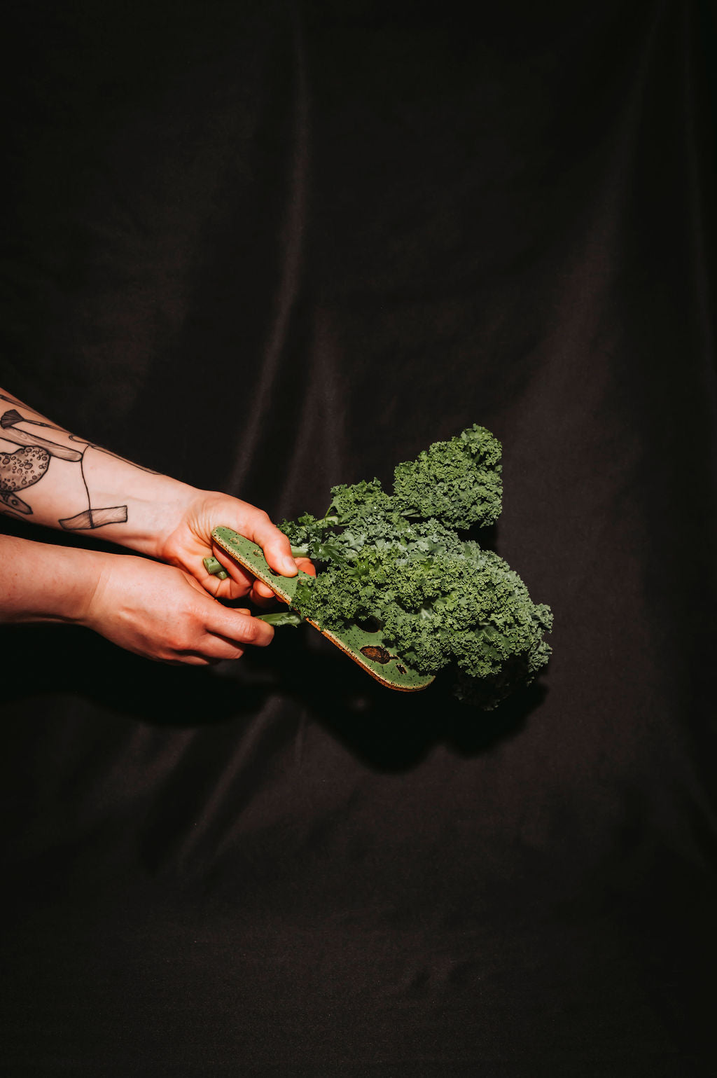 Person holding a bunch of green kale and using a ceramic herb stripper on a black background