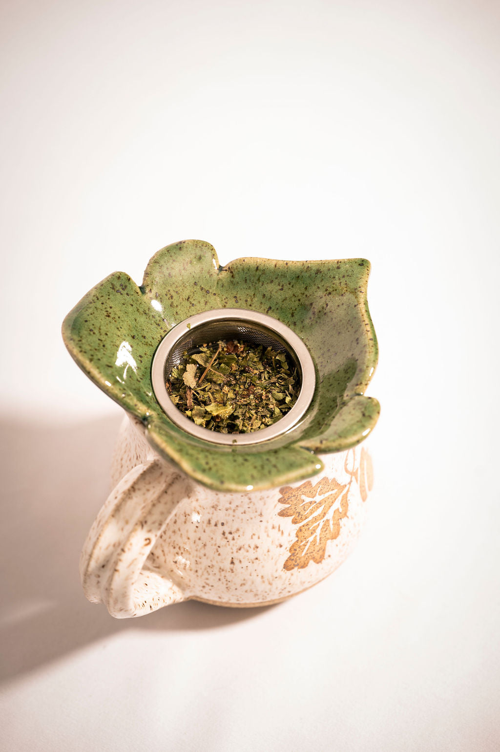 Ceramic tea infuser with green leaf design on a white mug. Shot from above to show leaves steeping in tea strainer.
