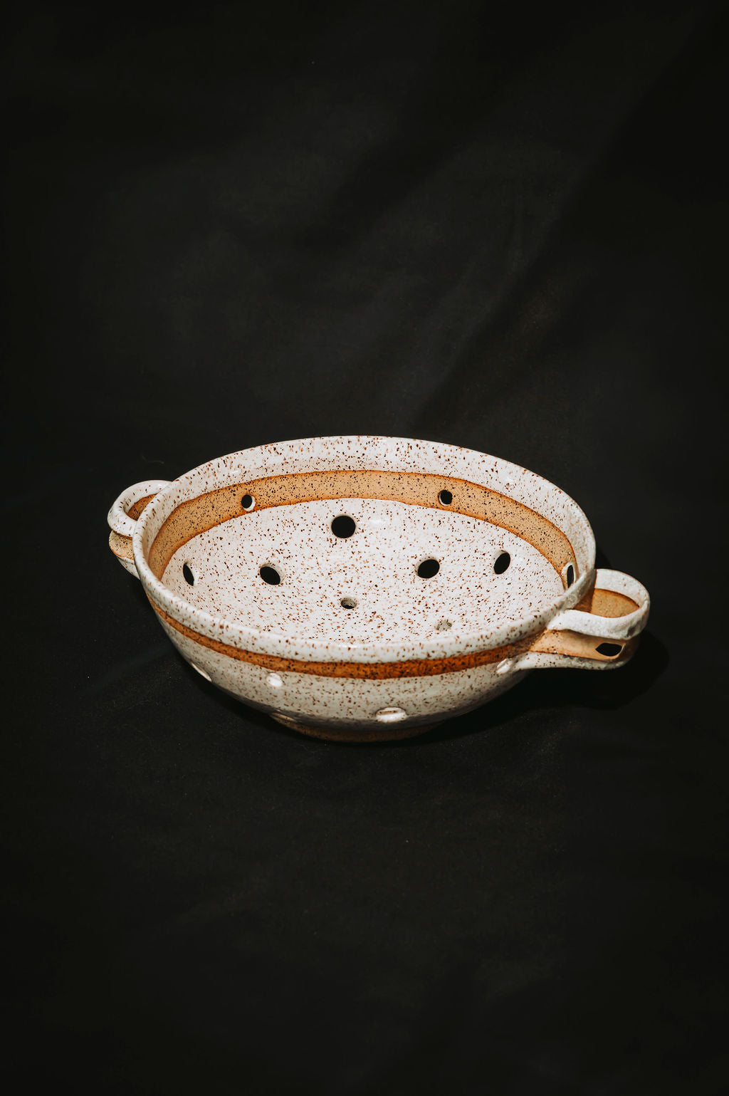 White ceramic colander with speckled pattern on a black background