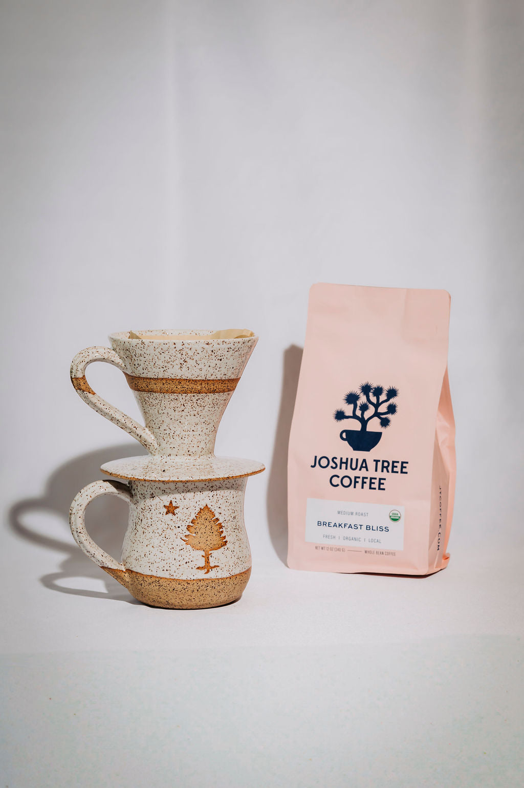 Ceramic coffee pourover sitting on a mug with a pink 'Joshua Tree Coffee' bag next to it on a white background
