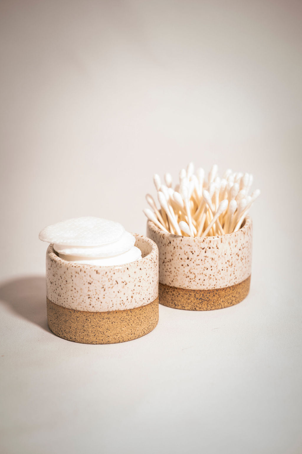 Two speckled white ceramic ramekins holding q-tips and cotton rounds.