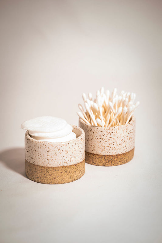 Two speckled white ceramic ramekins holding q-tips and cotton rounds.