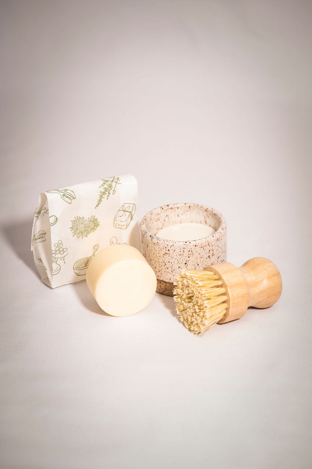 Set of eco-friendly cleaning products including a soap bar, brush, and container on a light gray background