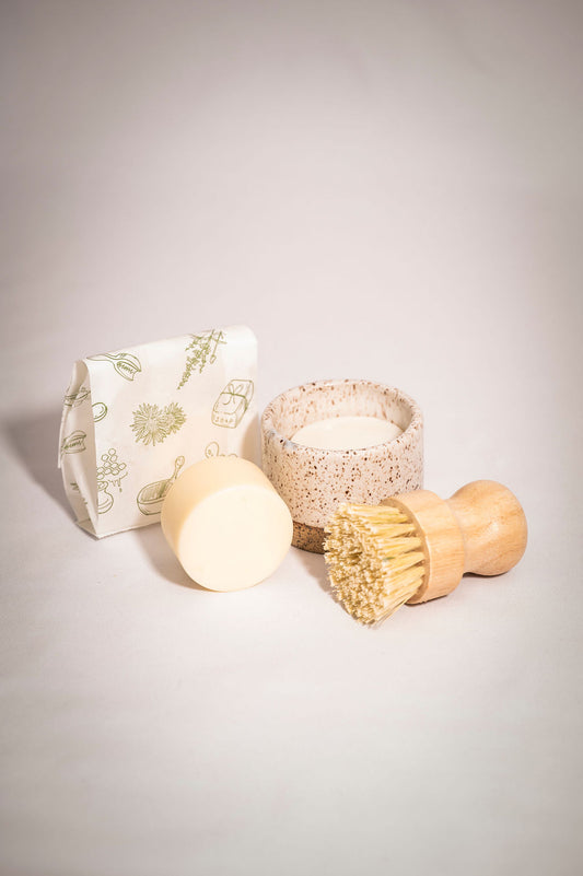 Set of eco-friendly cleaning products including a soap bar, brush, and container on a light gray background