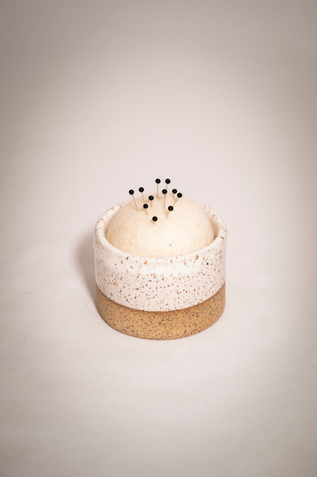 White speckled ceramic tumbler with a wool pin cushion. 