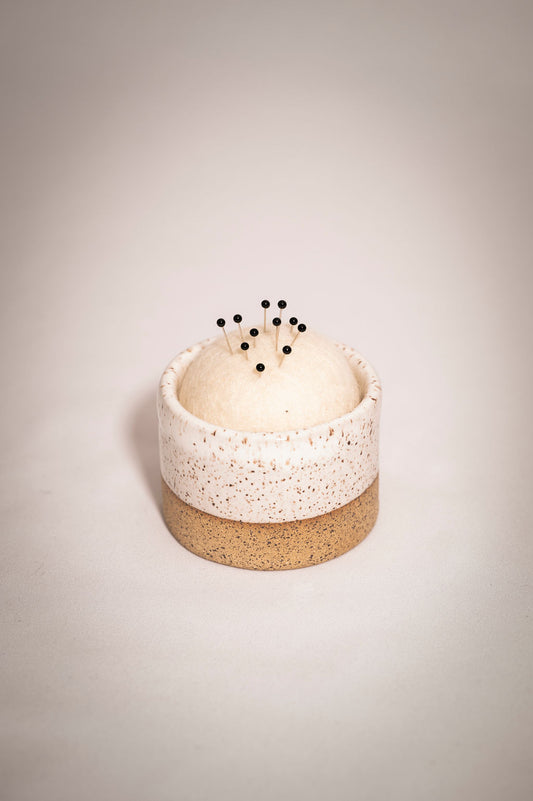 White speckled ceramic tumbler with a wool pin cushion. 