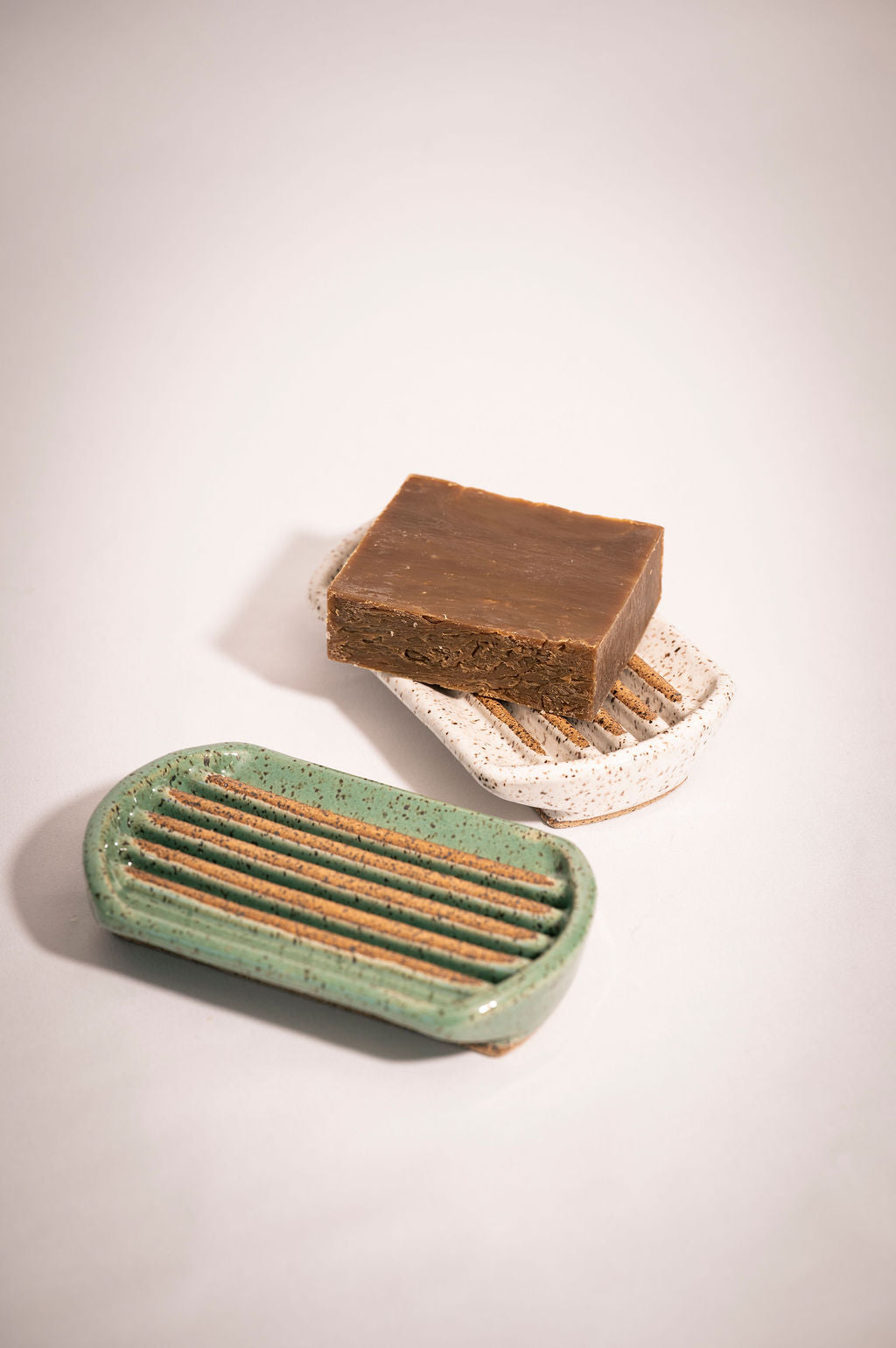 Two ceramic soap dishes with a brown bar of soap resting on the back dish,