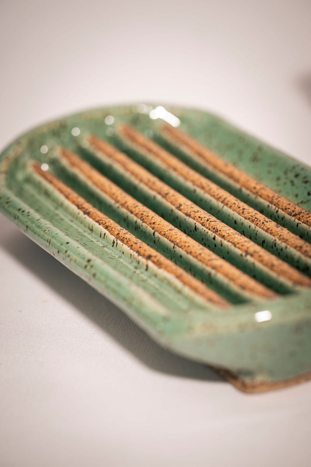 Close-up of a rectangular turquoise speckled ceramic soap dish with rounded edges showing the grooves the soap sits on.