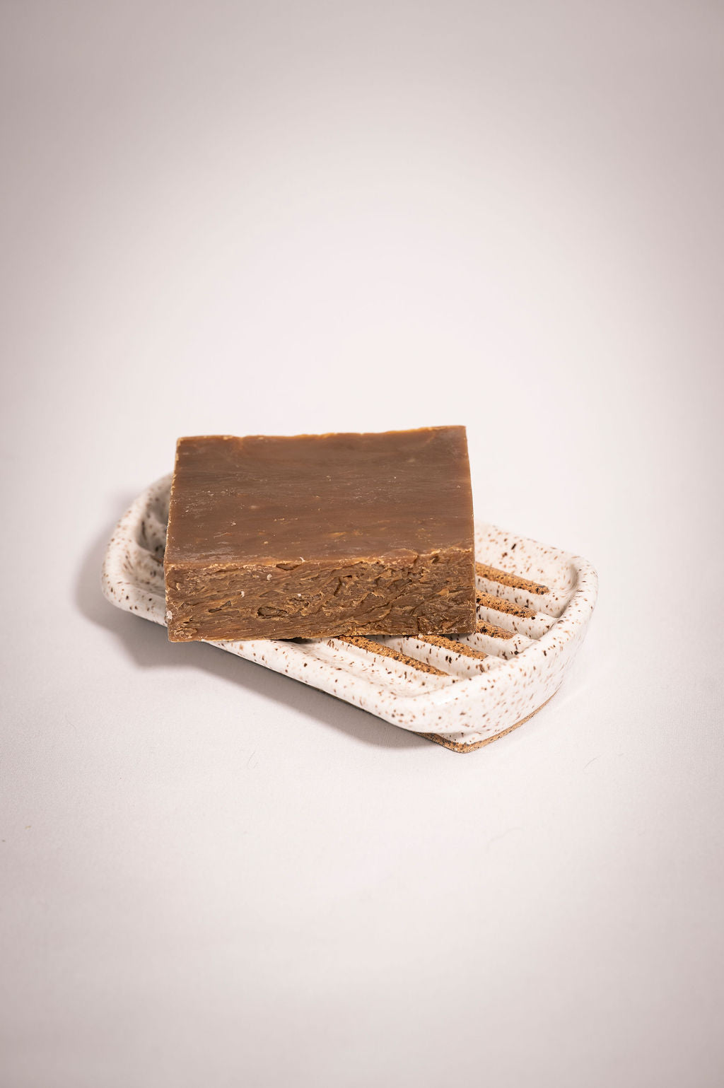 Bar of brown soap on a speckled white ceramic soap dish.