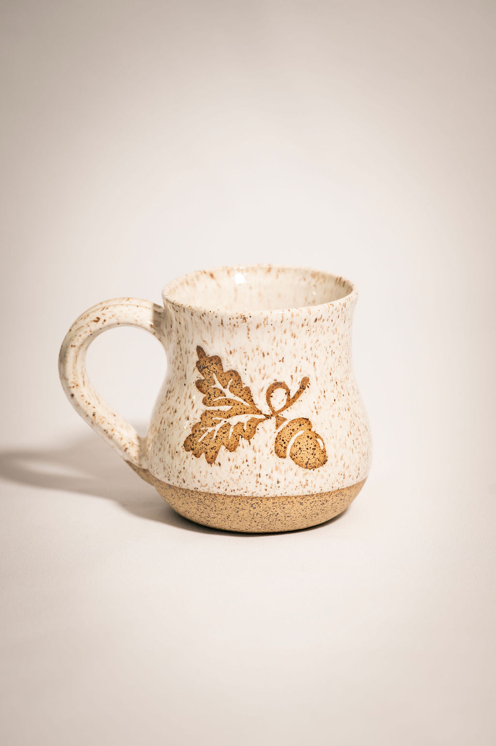 Speckled ceramic mug with leaf and acorn design on a beige background