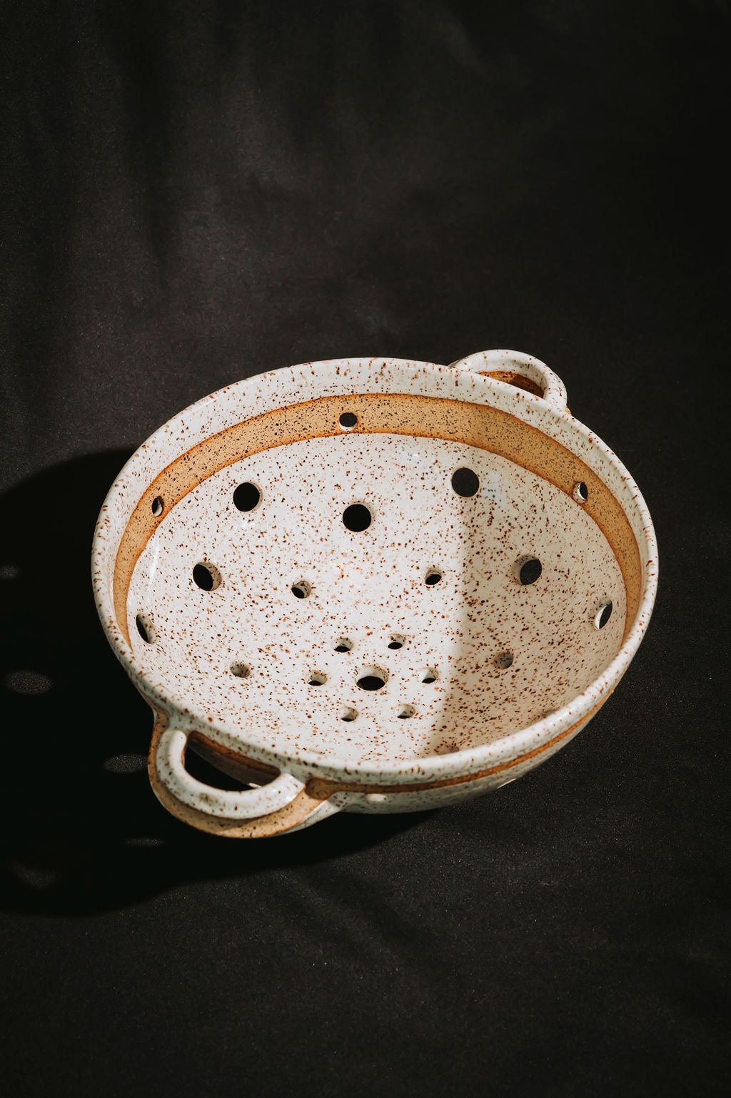 Ceramic colander with speckled pattern on a dark background