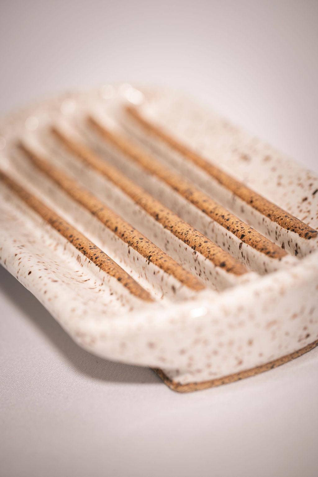 Close-up of a rectangular white speckled ceramic soap dish with rounded edges showing the grooves the soap sits on.