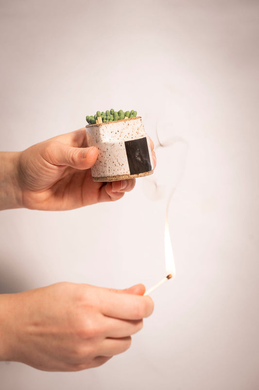 Person holding ceramic match holder and striking a match against the side.