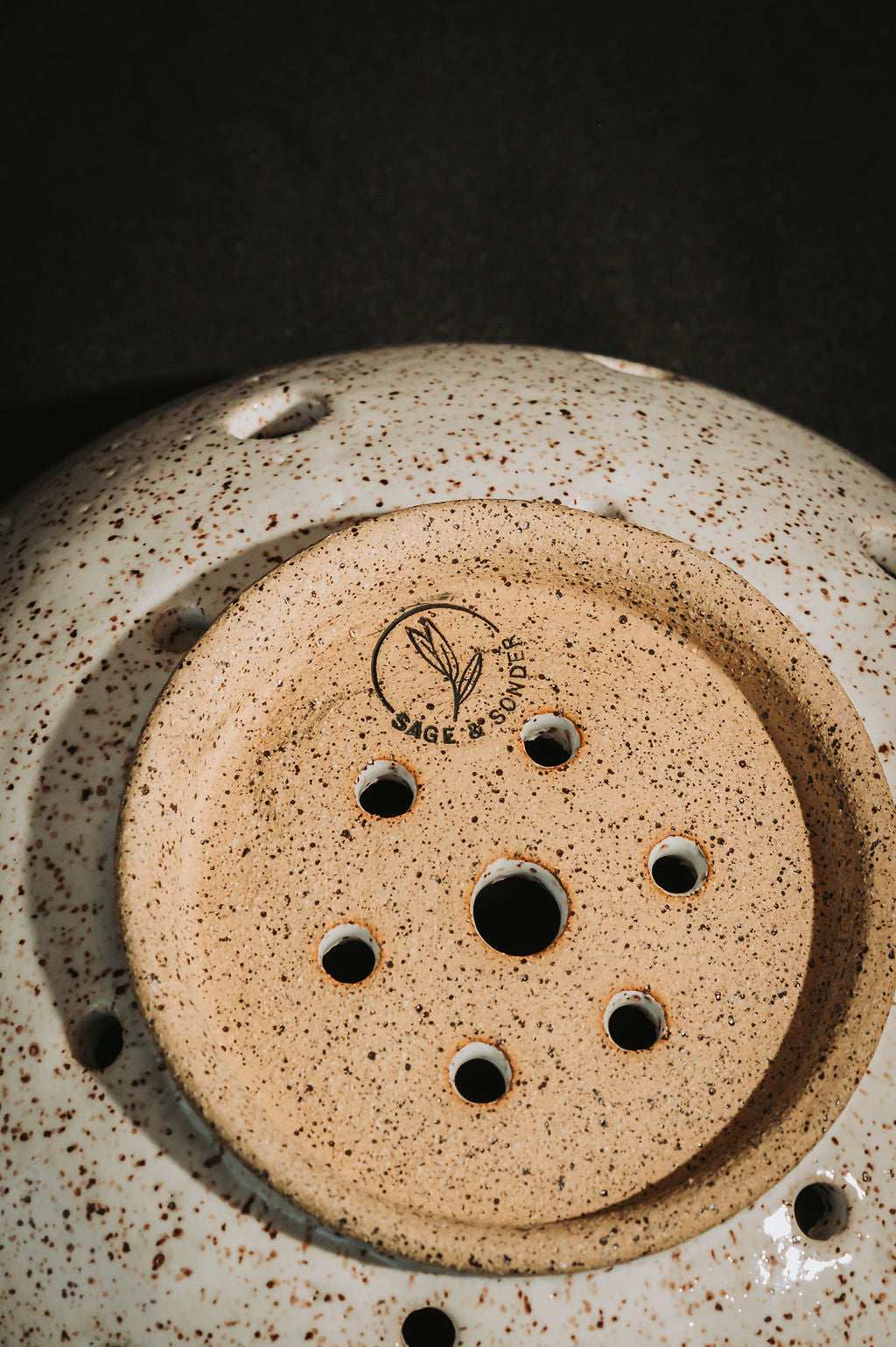 Close-up of the bottom of a ceramic berry bowl with speckled design and brand logo.