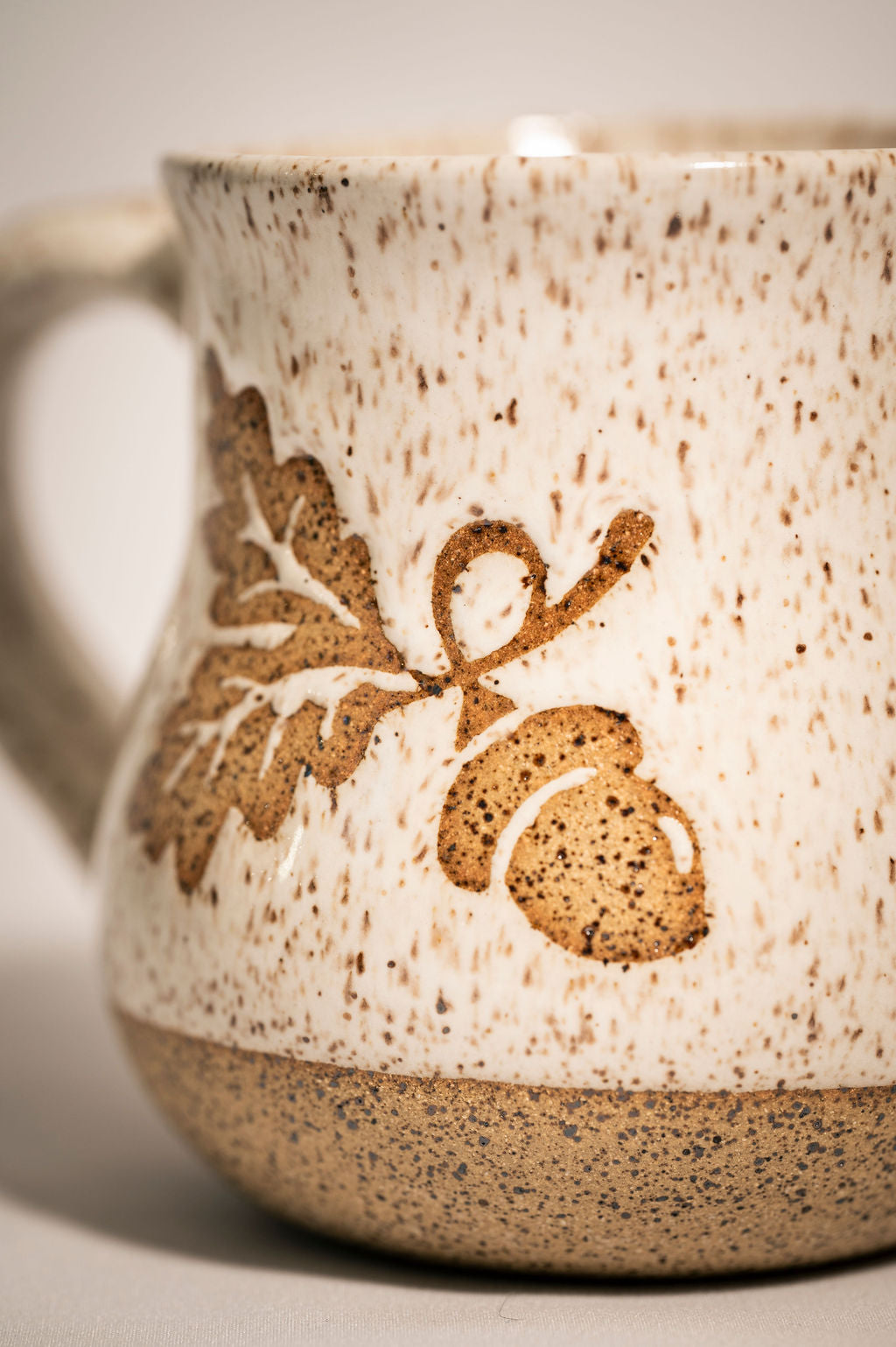 Close-up of a peckled ceramic mug with leaf and acorn design.