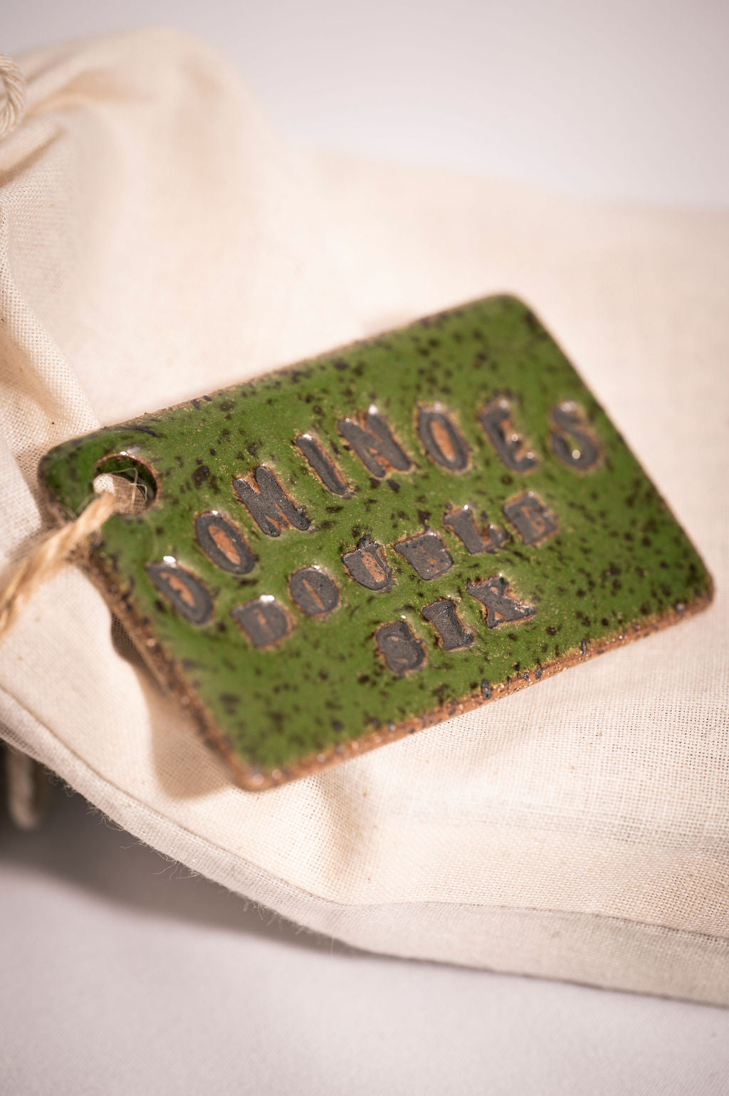 Green glazed ceramic tag with 'DOMINOES DOUBLE SIX' text on a beige background.