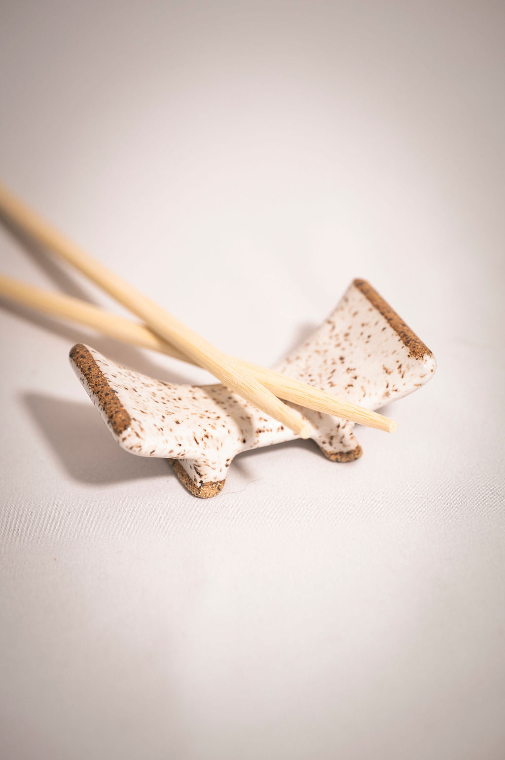 White speckled ceramic chopstick rest with chopsticks resting on the bottom curve.