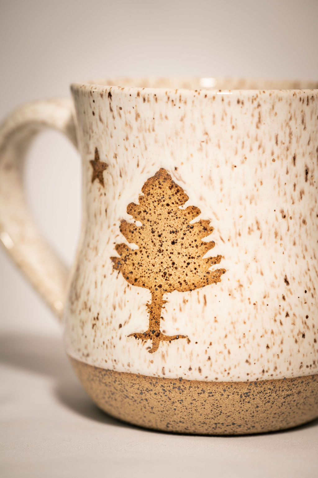 Close up of a ceramic white speckled mug with a maine state tree design 