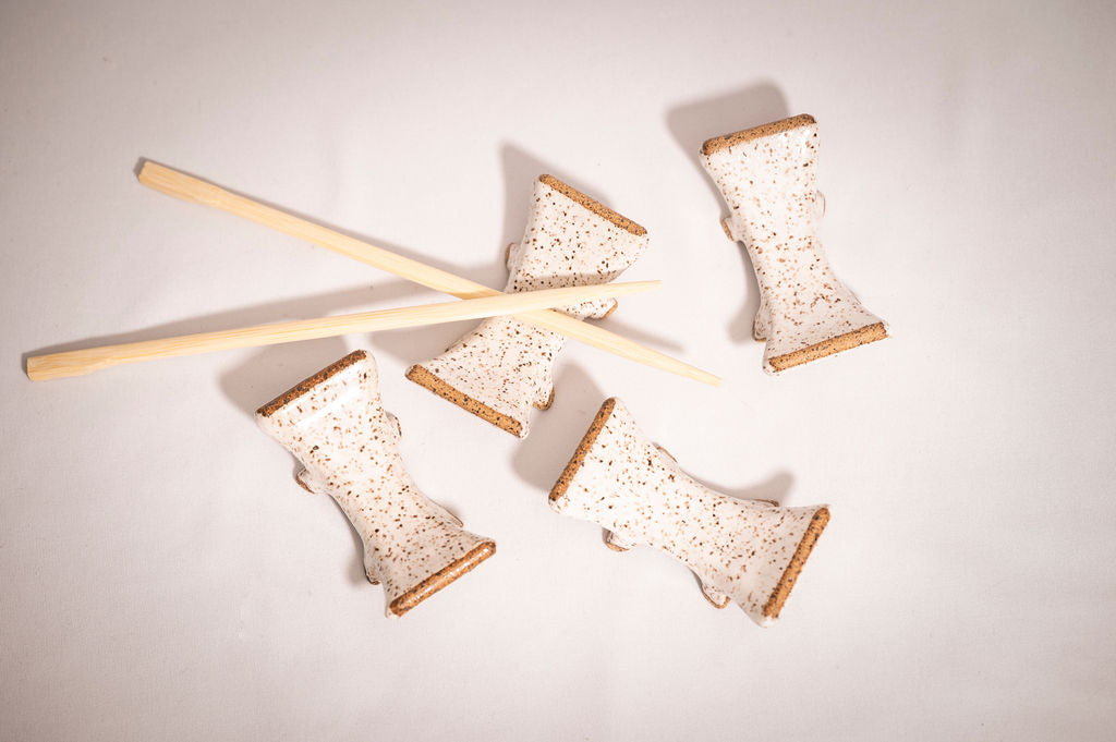 Set of four white speckled ceramic chopstick rests with a pair of chopsticks resting on one as an example.