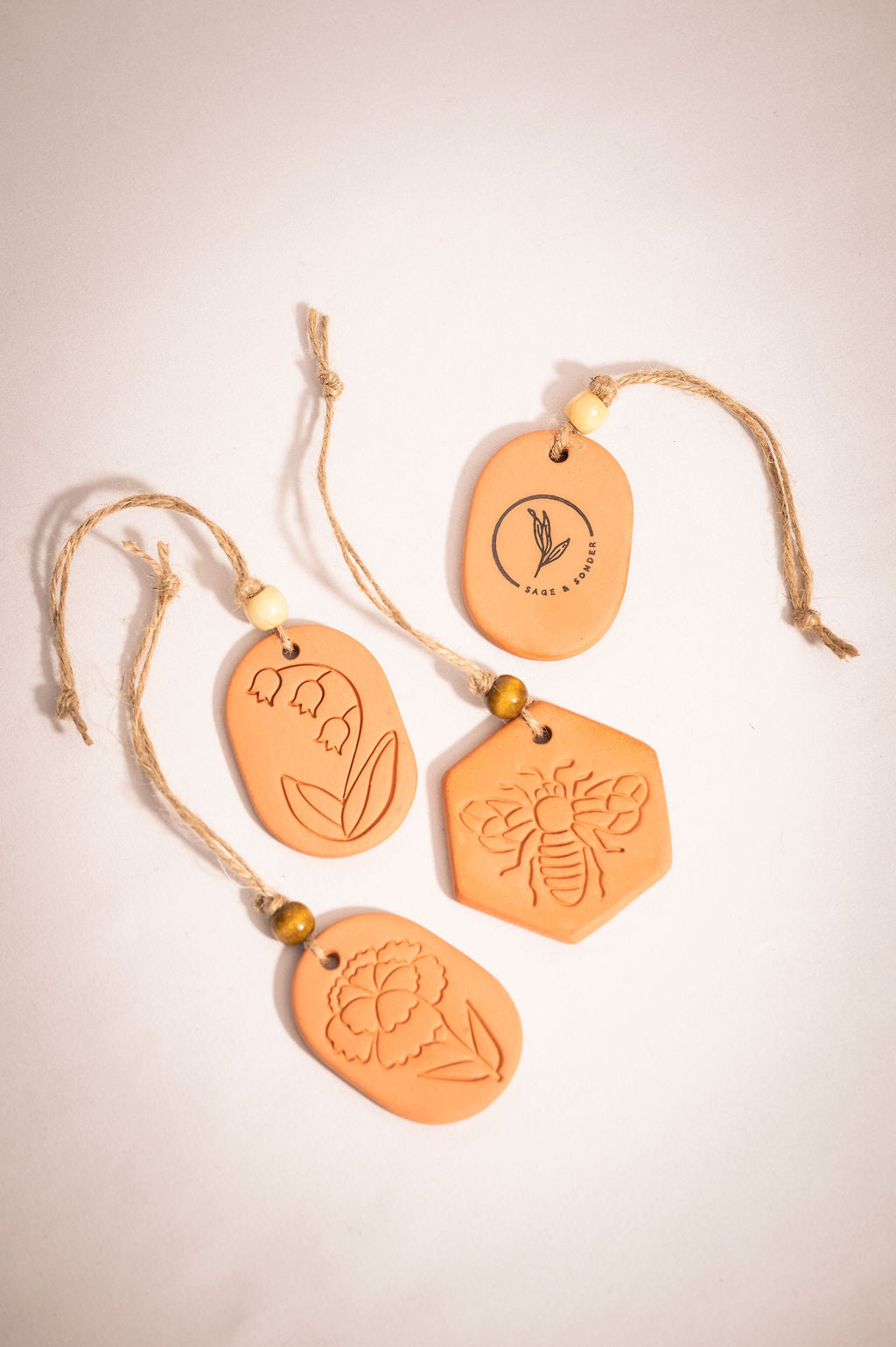 Four terracotta clay diffusers resting on a table with various nature inspired designs stamped onto the diffusers. 