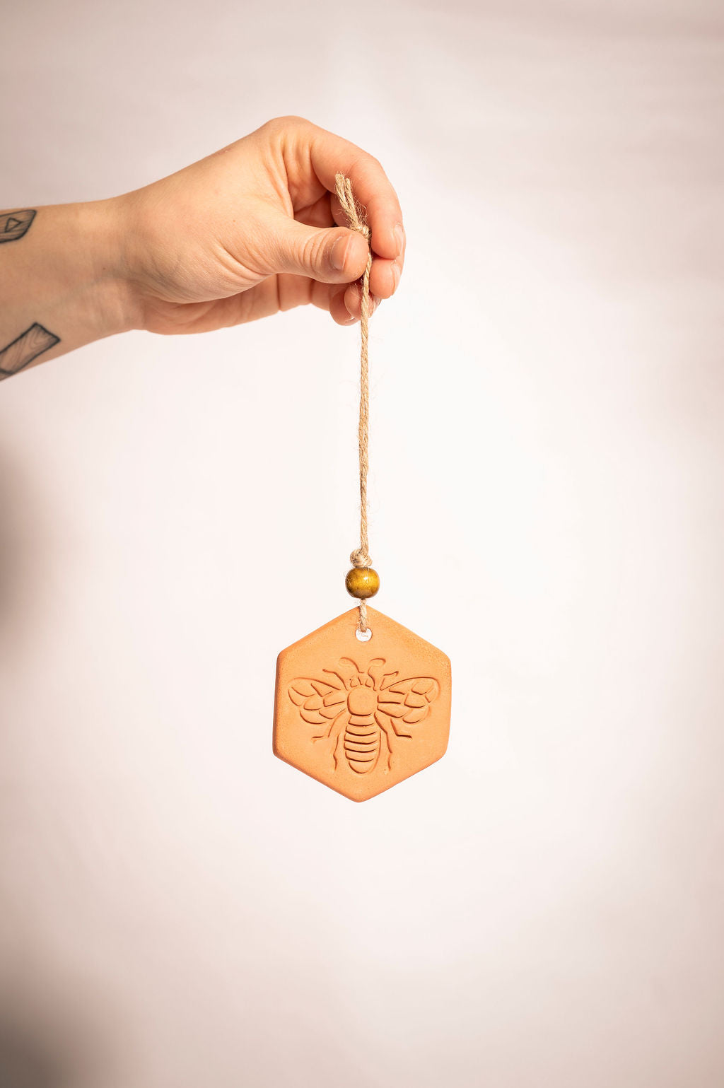 Person holding a hanging terracotta diffuser with a bee design.