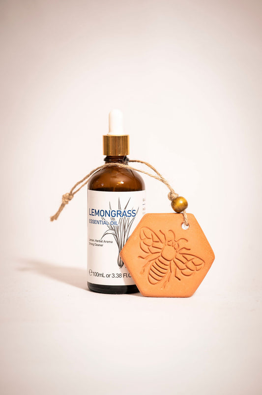Bottle of lemongrass essential oil with a stamped bee on a terracotta clay diffuser resting next to it. 