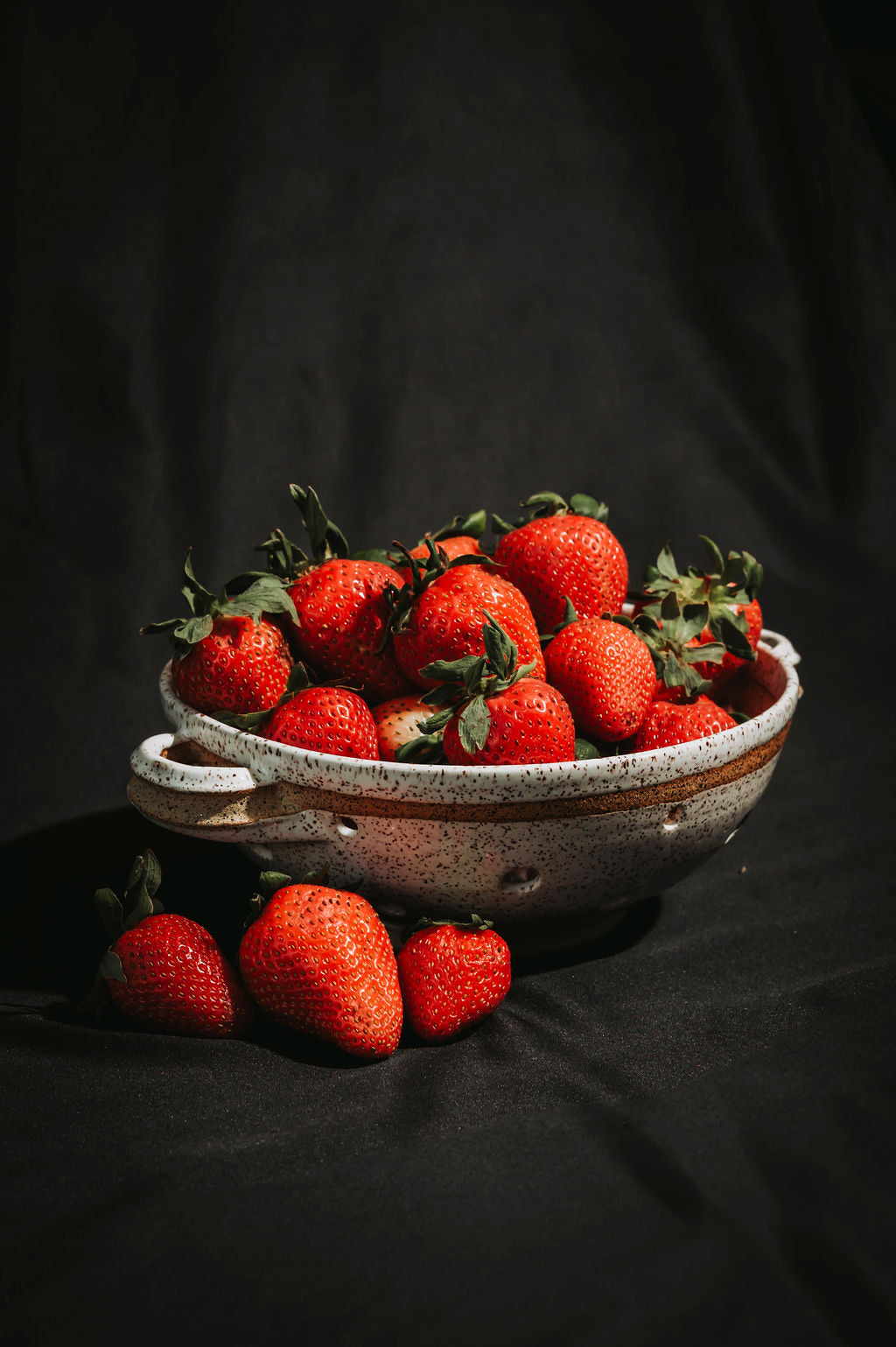 Bowl of strawberries in a white speckled ceramic colander on a dark background