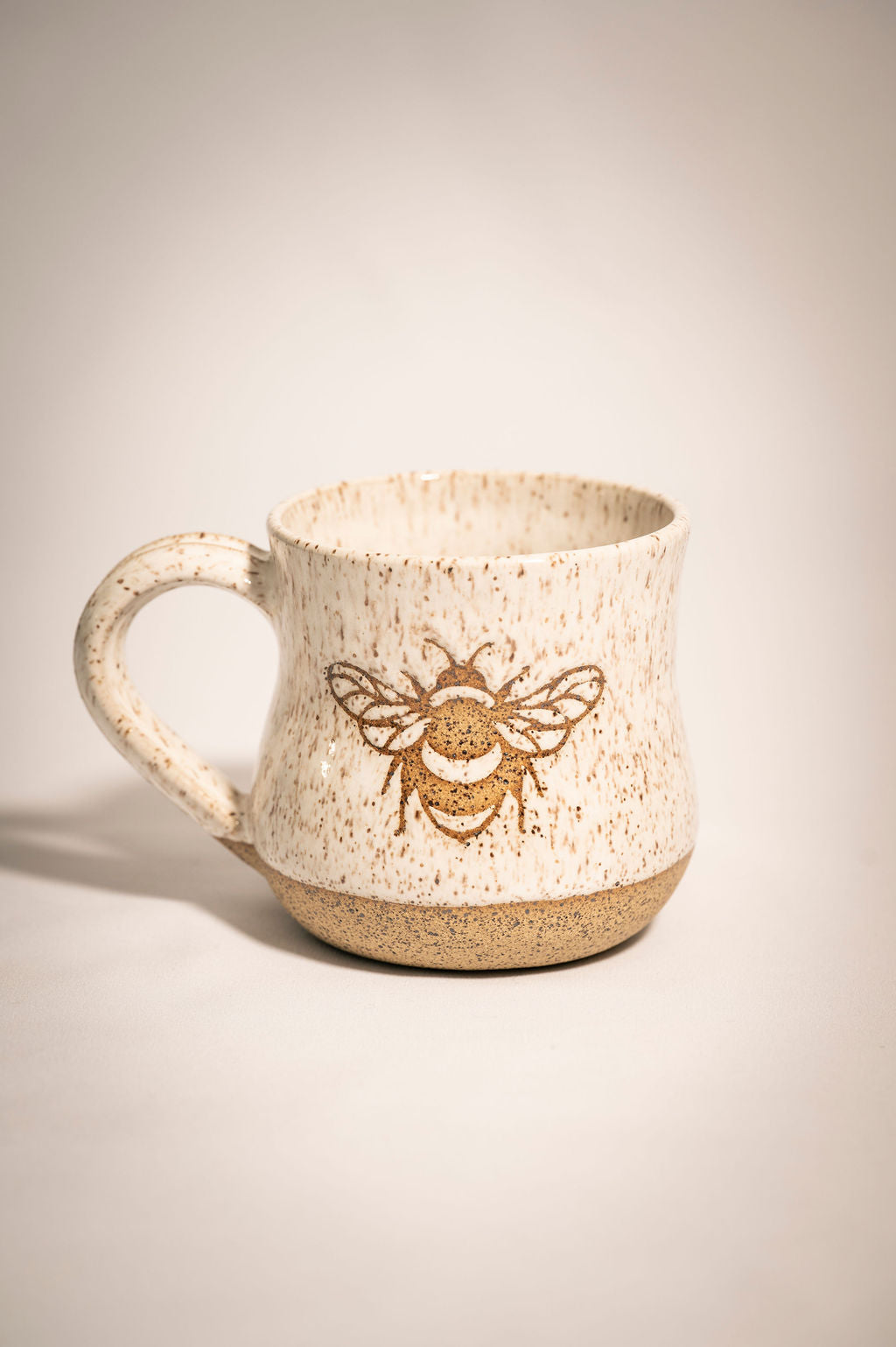 Speckled ceramic mug with a bee design on a beige background
