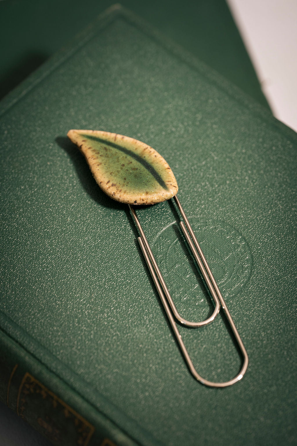 Leaf-shaped bookmark resting  on a green fabric bound book.