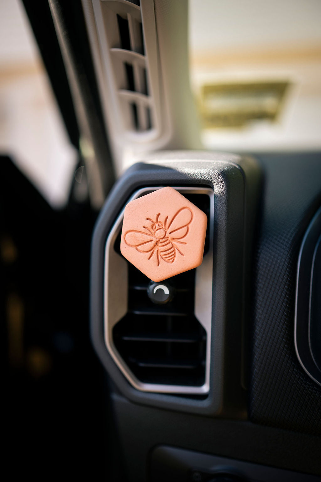 Terracotta clay diffuser stamped with a bee on a car air vent.