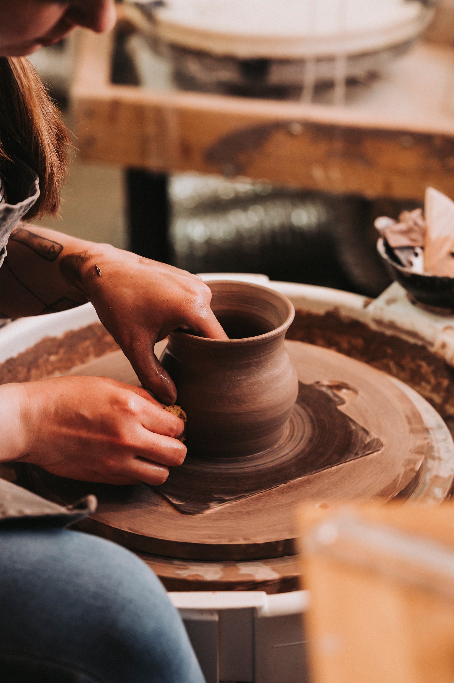 Person working with clay on a pottery wheel throwing a mug form