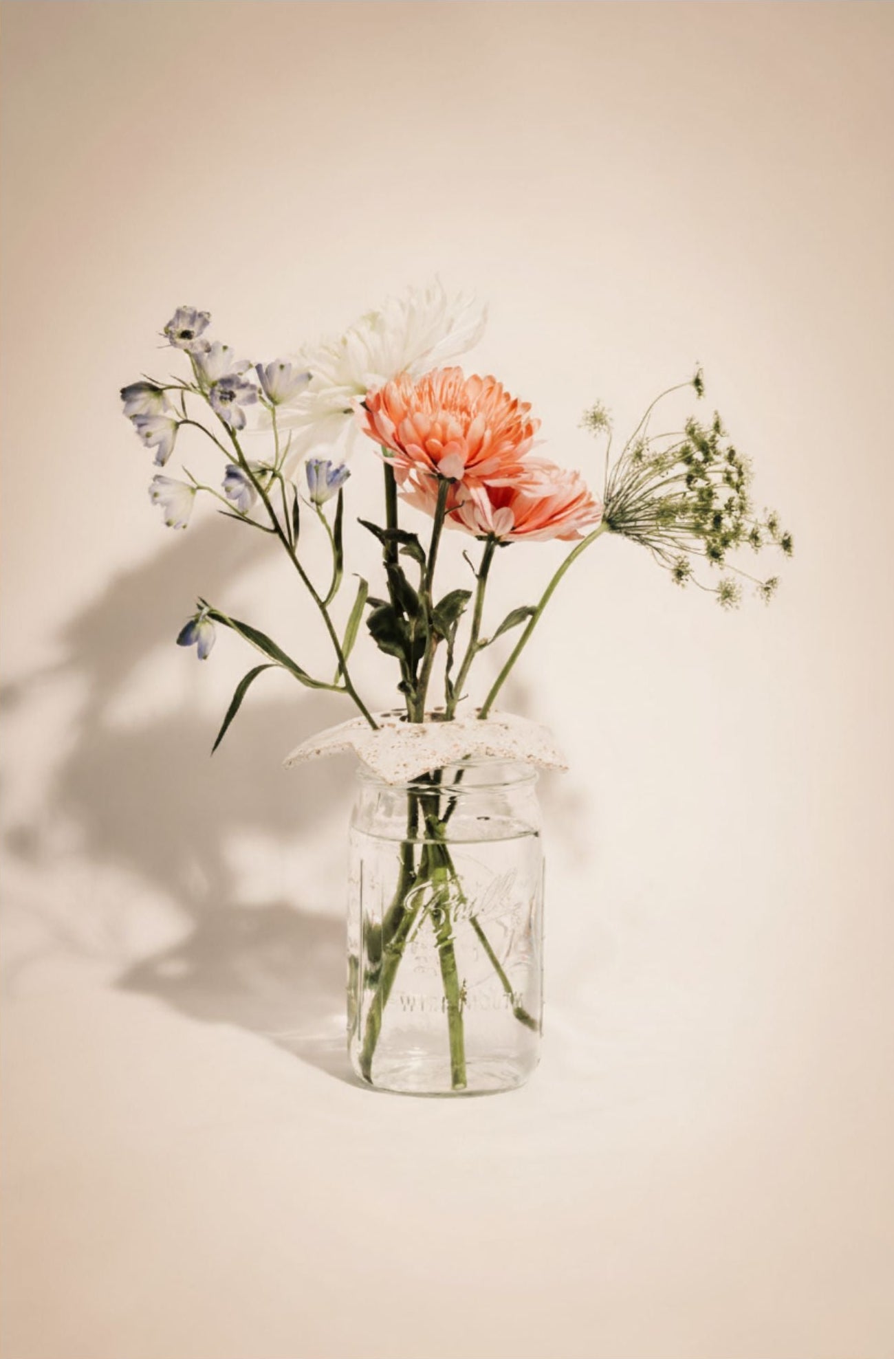 Clear glass mason jar with a ceramic flower frog with flowers on a beige background